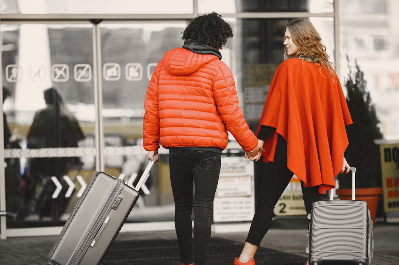 A couple holding hands with luggage, entering an airport for a travel journey.